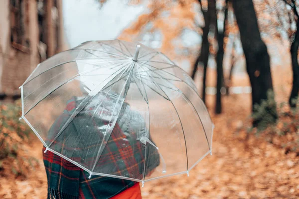 Retrato de una mujer adulta con un sombrero blanco y una bufanda caliente bajo un paraguas transparente en un parque de otoño al aire libre — Foto de Stock