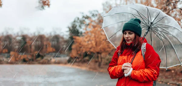Όμορφο κορίτσι κρατώντας μια διάφανη ομπρέλα κατά τη διάρκεια της βροχής το φθινόπωρο νεφελώδης καιρός το φθινόπωρο. Γυναίκα σε κόκκινο αδιάβροχο φθινοπωρινό σακάκι στην πόλη — Φωτογραφία Αρχείου