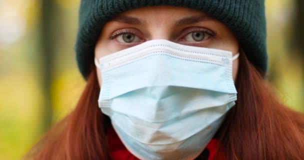 Porträtt av ung flicka i en skyddande medicinsk mask och varma kläder tittar in i kameran. Turist i höstskogen — Stockvideo