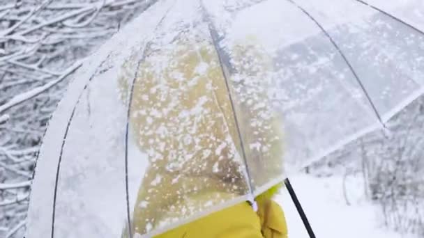 Diviértete caminando. Mujer adulta feliz en ropa de abrigo amarillo con paraguas transparente y sonrisas bajo la nieve pesada. — Vídeos de Stock