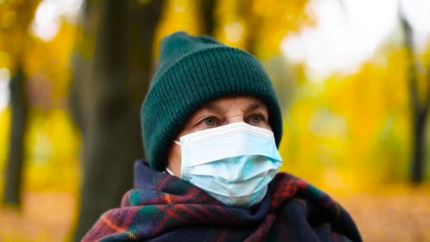 Donna caucasica 50 anni in maschera medica guardando dritto alla macchina fotografica mentre in piedi all'aperto nel parco della città. Pandemia — Video Stock