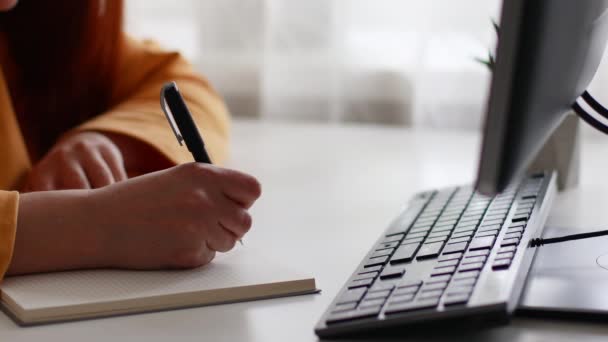 Młoda dziewczyna siedzieć pulpit pc trzymać pióro pisać notatnik w domu biuro wewnątrz — Wideo stockowe