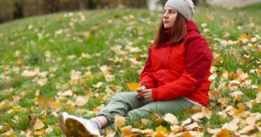 Güzel beyaz elbiseli kız sonbaharda parkta eğleniyor. Sarı bir yaprağı tutan bir kız.