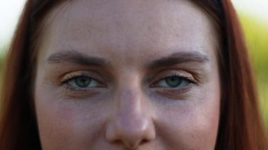 Beyaz tenli güzel bir kadın neşeyle gülümserken gün batımında şehir parkındaki kameraya bakar.