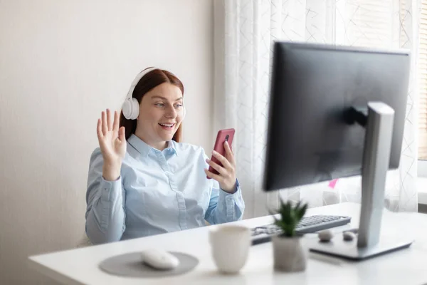 Hezká mladá žena používající mobilní telefon při práci s PC doma. Online videokonference. — Stock fotografie