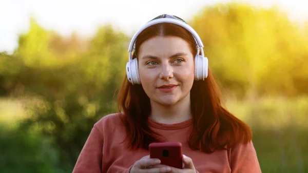 Krásná tisíciletá žena poslouchající hudbu se sluchátky. Student používající chatování mobilních telefonů. — Stock fotografie