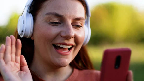 Student using mobile phone, having video chat and smiling while walking in spring park — Stock Photo, Image