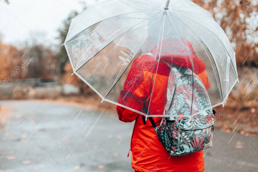 Woman in a red jacket walks around the city under a transparent umbrella on a cold rainy day