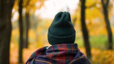 Back view of old tourist traveler girl with a warm scarf walks in a beautiful autumn gold forest