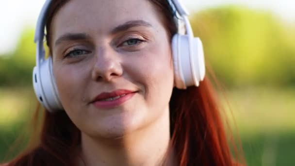 Mujer caucásica milenaria con auriculares blancos escuchando música con los ojos cerrados. Estilo de libertad de las personas. — Vídeos de Stock