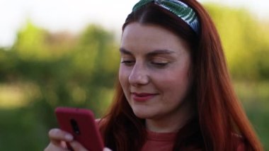 Dışarıda açık havada akıllı telefon kullanan bin yıllık gülümseyen bir kadının portresi. Çevrimiçi iletişim