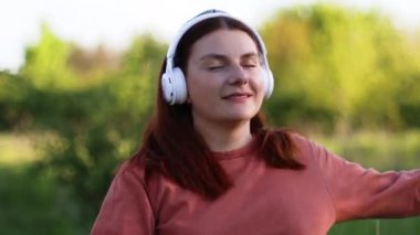 Mutlu komik kadın sokakta dans edip kulaklıkla müzik dinliyor.
