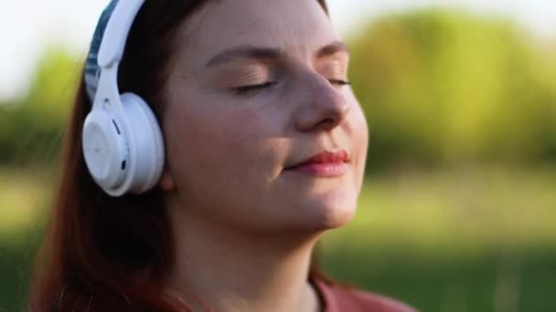 Blank gelukkig vrouw dragen witte hoofdtelefoon luisteren naar muziek met ogen dicht op straat buiten. — Stockvideo