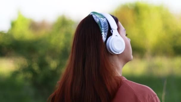 Mujer escuchando música con auriculares en la posición trasera mirando hacia atrás — Vídeos de Stock