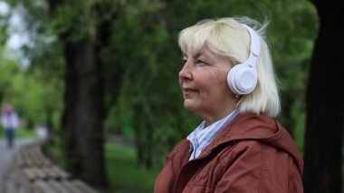 Relax woman face using smartphone and listening music by white headphones on street outdoors in city park.