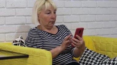 Portrait blonde woman using smartphone. Young girl holding cellphone, chatting in social networks, sitting on couch in living room.