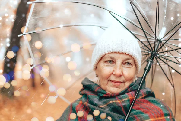 Retrato de una mujer adulta con un sombrero blanco y una bufanda caliente bajo un paraguas transparente en un parque de otoño al aire libre —  Fotos de Stock
