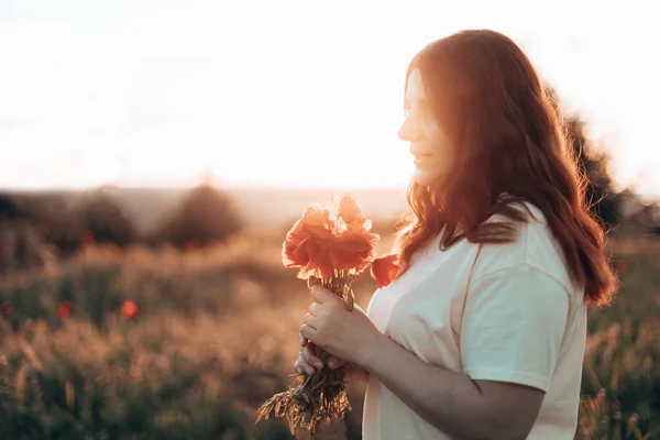 Jovem mulher ruiva feliz com flor em um campo de papoula florescendo ao sol. — Fotografia de Stock