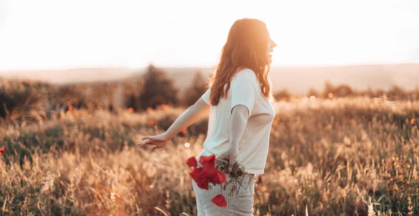 Joyeux beau fille avec bouquet de fleurs dans un champ de pavot au coucher du soleil. Souriante fille marche au coucher du soleil et rit. — Photo