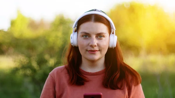 Jolie fille heureuse écoutant de la musique avec des écouteurs. Étudiant utilisant un téléphone mobile, ayant un chat vidéo — Photo