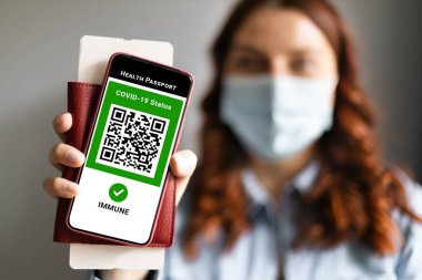 Young girl wearing a face mask holding a passport, ticket pass and smartphone with digital health passport app. Covid-19 Health Passport.
