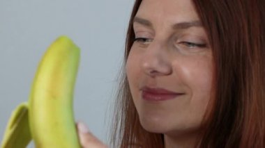 Taze muz soyan, gri arka planda sağlıklı meyvenin tadını çıkaran Kafkasyalı genç kadına yakın durun..