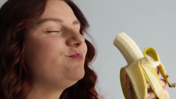 Primo piano di gioiosa affascinante donna caucasica mordere banana matura gialla e guardando nella fotocamera. Femmina faccia mangiare banana — Video Stock