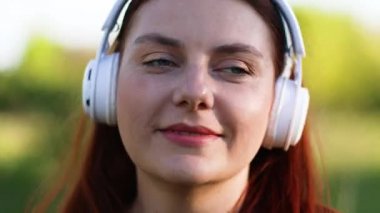 Beyaz kulaklık takan, sokakta gözleri kapalı müzik dinleyen ve dışarıda müzik dinleyen beyaz, mutlu bir kadın..
