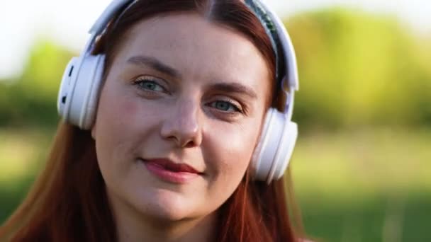 Blank gelukkig vrouw in hoofdtelefoon lopen op straat en luisteren naar muziek buiten. — Stockvideo