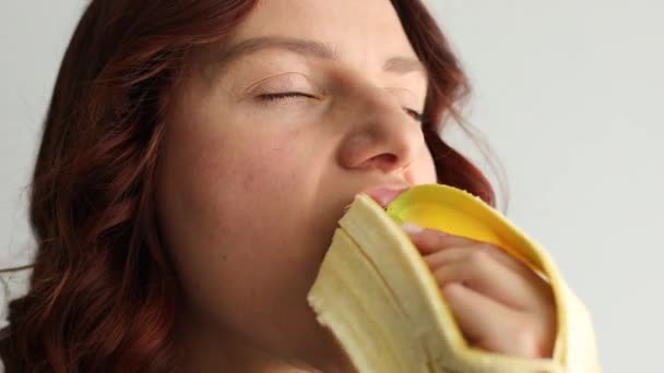 Primo piano di bella giovane donna caucasica che morde banana matura gialla. Femmina faccia mangiare banana — Video Stock