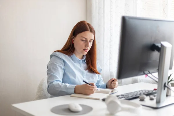 Happy stylish woman remote working from home distance office on pc taking notes. Smiling business lady using computer watching webinar