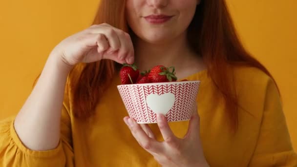Närbild av glada charmiga kaukasiska provsmakning en läcker jordgubbe över gul bakgrund — Stockvideo