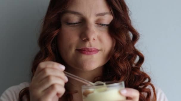 Positivo encaracolado caucasiano menina comendo deliciosa sobremesa cremosa, apreciando o gosto no fundo cinza — Vídeo de Stock