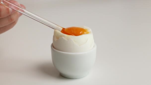 Brown egg in egg cup. Eat a boiled egg from a cracked eggshell with a glass spoon. — Stock Video
