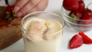 Bir kadın eli, mutfaktaki tiramissa tatlısını süslemek için tahta bir tahtada olgun çilek kesiyor. Sağlıklı gıda konsepti