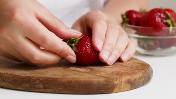 Жіночі руки розривають хребет з полуниці і розрізають ягоду на дерев'яній дошці на кухні. Концепція здорової їжі — стокове відео