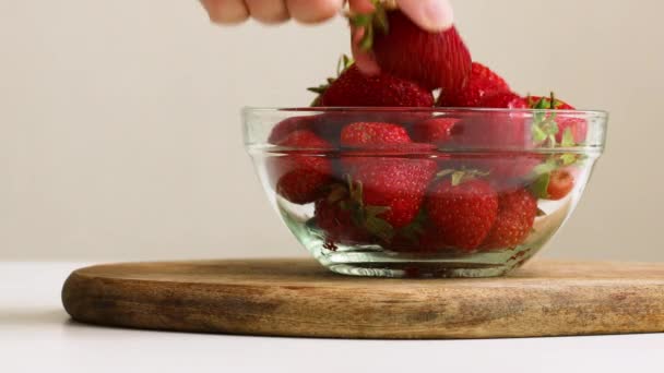 Vrouwelijke hand neemt rijpe aardbeien uit een glazen schaal op een witte tafel in de keuken. Gezond voedselconcept — Stockvideo