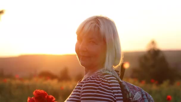 Adulto donna caucasica turista con zaino e papavero mazzo di fiori al tramonto nel campo. vacanze estive. Ragazza felice con i capelli biondi godendo il sole. — Video Stock
