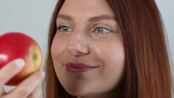 Retrato de mujer hermosa sosteniendo manzana roja madura fresca en la mano y huele fruta orgánica aislada sobre fondo gris. — Vídeo de stock