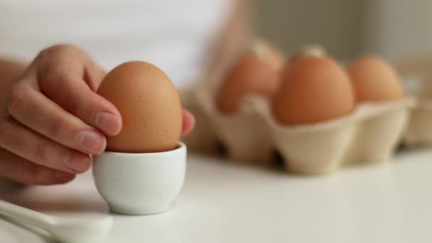 Рука людини бере варене яйце з яєчної чашки на білому столі — стокове відео