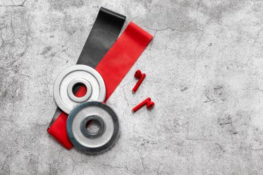 Kırmızı lastik jimnastik sakızı, dambıl krepleri, beton arka planda kablosuz kulaklıklar. Çevrimiçi Fitness programı. Evde çevrimiçi çalışma