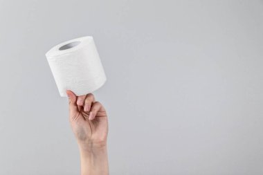 Kadın eli, arka planı gri ve fotokopi alanı olan bir tuvalet kağıdının yumuşak rulosunu tutuyor. Reklam için en düşük kompozisyon, makale