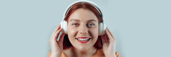 Glad glad glad leende ung kvinna i vita hörlurar lyssna på musik på en grå bakgrund — Stockfoto