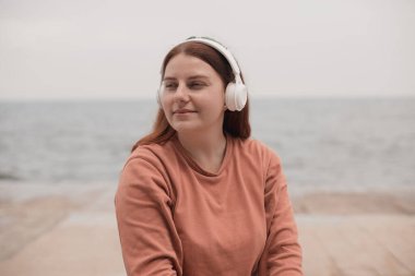 Genç kız portresi, deniz kenarında kablosuz kulaklıklarla meditasyon yapıyor.