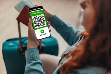 Coronavirus çalışanı elinde pasaport, bilet kartı ve covid-19 salgını sırasında seyahat için dijital sağlık pasaportlu akıllı telefon tutuyor..