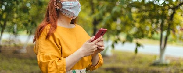 COVID-19 Coronavirus Fiatal nő visel orvosi maszk használ smartphone app a városi parkban világjárvány idején — Stock Fotó