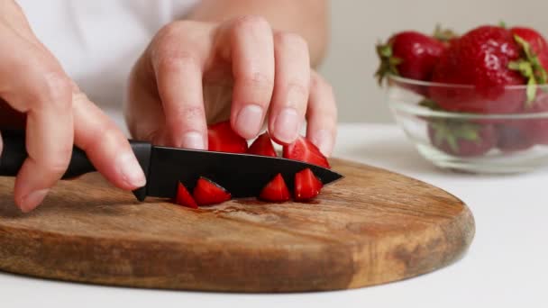 Жіноча рука розрізає стиглу полуницю на дерев'яній дошці на кухні . — стокове відео