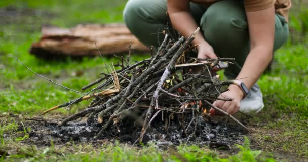 Una joven con un fósforo enciende una rama para la fogata en el bosque. Acogedor fuego. Camping de otoño — Vídeo de stock