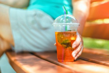 Kadın eli aperol spritz tutuyor, Evergreen Park 'taki ahşap bankta oturuyor, dinlenme zamanının tadını çıkarıyor. Sağlıklı gıda konsepti