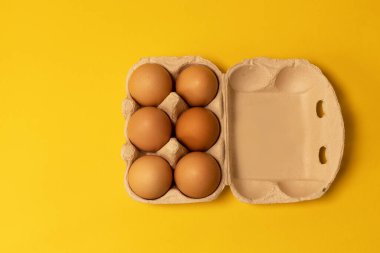 Sarı zemin üzerinde karton kutuda kahverengi tavuk yumurtaları, düz yatış, kopyalama alanı.